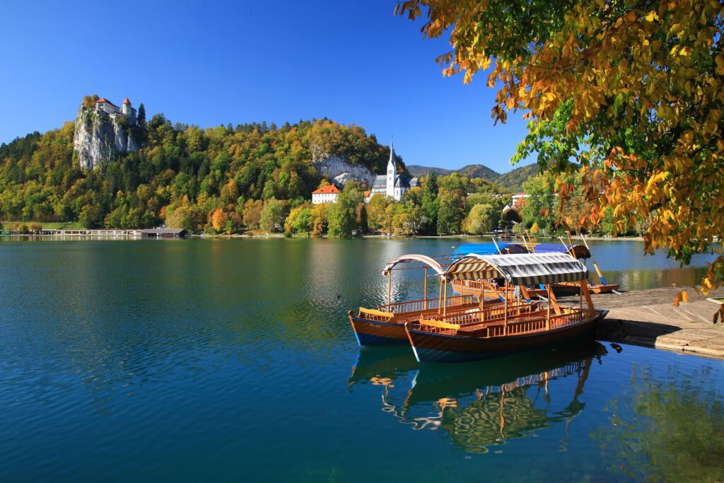 Traditional pletna boats on Lake Bled in autumn with the castle above